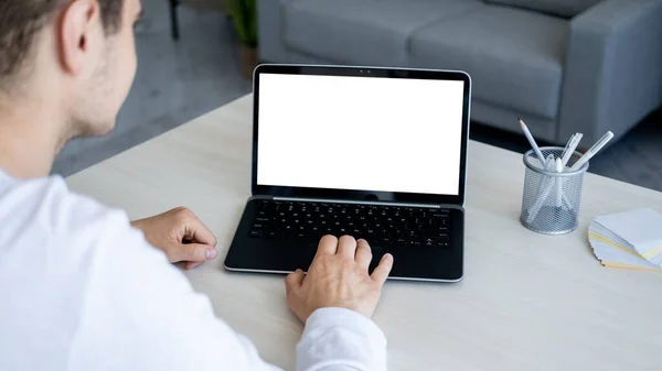 Online conference. Distance work. Computer mockup. Unrecognizable man sitting desk with laptop blank screen in light room interior.