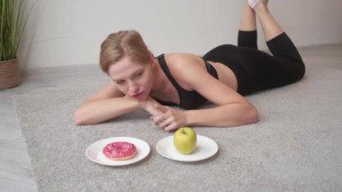 Fitness yemeği seçimi. Sağlıksız diyet. Tatlı abur cubur. Mutlu atletik kadın yeşil elma meyvesi yerine lezzetli tatlı çörekleri topluyor..