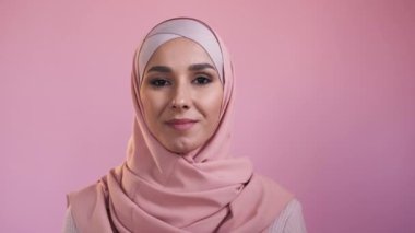 Happy muslim woman. Positive attitude. Traditional outfit. Portrait of joyful smiling young female face in hijab isolated on pink studio background.