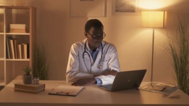 TeleHealth video görüşmesi. Sanal check-up. Mesafe randevusu. Modern işyerinde geç saatlere kadar çalışan laptopla kendine güvenen erkek doktor hastaya danışmanlık yapıyor..