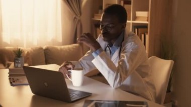 Doktor Uykusuzluk. Sağlıklı yaşam tarzı. Profesyonel yorgunluk. Yorgun, uykulu erkek doktor. Laptop kullanıyor. Kahve içiyor. Gözlüklerini çıkarıyor..