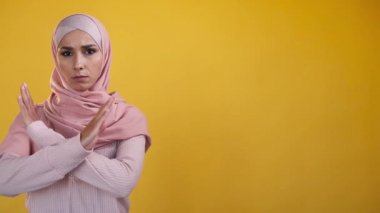 No rejection. Stop gesture. Forbidden topic. Strict frowning refusing woman in hijab showing crossed arms denial sign isolated on yellow copy space background.