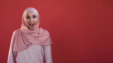 Amazed woman. Wow face. Advertising background. Surprised excited female in hijab shocked with unbelievable offer isolated on red empty space.