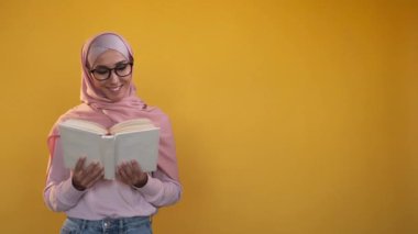 Woman student. Book reading. University education. Intelligent happy learning girl in hijab isolated on yellow copy space studio background.