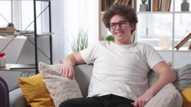 Vacation holiday. Satisfied man. Enjoying moment. Happy relaxed guy in spectacles feeling good sitting sofa with travelling suitcase in light room interior.