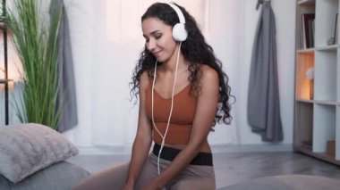 Music gadget. Playlist joy. Song listening. Happy millennial carefree woman enjoying audio tune in headset dancing with phone at home.