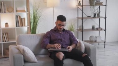 Remote job. Working from home. Freelancer lifestyle. Smart confident business man using laptop sitting on couch in modern living room interior.