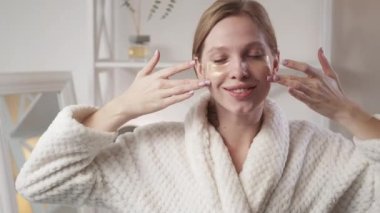 Cilt tazeleme. Güzellik bakımı. Yaşlanma karşıtı kozmetoloji. Yüzü temiz gülümseyen tatmin olmuş bir kadın. Açık evdeki göz bantlarının altına altın rengi kolajen jel sürüyor..