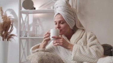Sabah içkisi. Spa detoksu. Haftasonu rahatlama. Bardaklı, mutlu, gülümseyen bir kadın hafif modern ev içinde duştan sonra bitkisel çay aromasının tadını çıkarıyor..