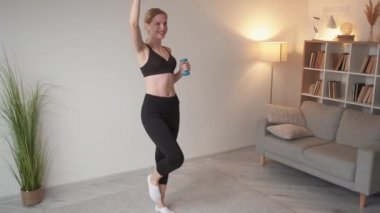 Evde fitness. Kapalı alan sporu. Aktif yaşam tarzı. Dambıllı, gülümseyen bir atletik kadından esinlenerek modern oturma odasında, iç mekanda, boş alanlarda eğitim gördü..