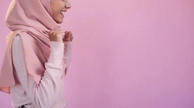 Heyecanlı kadın. Vay canına. Reklam önerilir. Mutlu bayanları kutlarken tesettür içinde pembe boş arkaplanda baş parmaklarını gösteriyor..