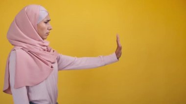 Stop refusal. Denying woman. No gesture. Side view of rejecting female in hijab with outstretched hand showing decline sign isolated on yellow copy space background.