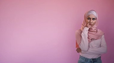 Pensive woman. Offer decision. Advertising background. Doubtful female in hijab with thoughtful expression thinking of choice isolated on pink copy space.