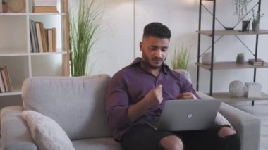 Virtual meeting. Video interview. Corporate telecommuting. Confident executive man discussing work using notebook sitting on couch at modern home office interior.
