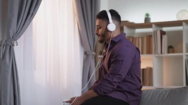 Music app. Morning playlist. Weekend inspiration. Relaxed guy enjoying listening audio in headphones drinking coffee at home interior with free space.