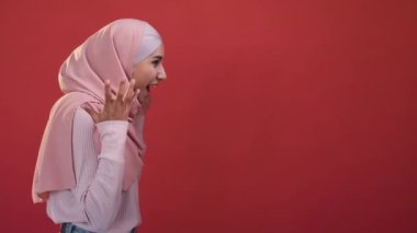 Crazy discount. Wow advertisement. Special offer. Side view amazed happy excited woman in hijab with omg face expression isolated on red empty space background.