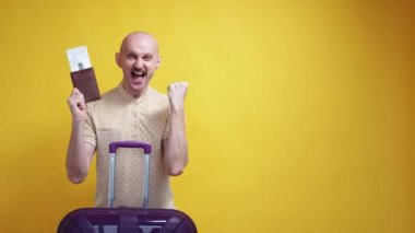 Happy holiday. Excited man. Vacation tour. Joyful guy with suitcase dancing with foreign passport and tickets expressing winner emotion yellow background.