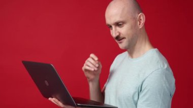 İnternetten alışveriş. Mutlu adam. Dijital teknoloji. Şaşırmış, tatmin olmuş, dizüstü bilgisayarla el ele tutuşmuş kırmızı arka plan..