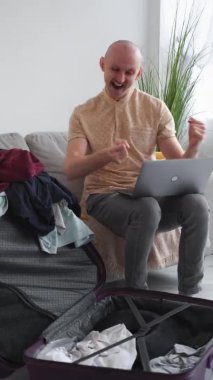 Yolculuk kazandı. Etkileyici bir adam. Çevrimiçi tur. Heyecanlı adam dizüstü bilgisayara bakıyor. Mutluluğunu ifade ediyor. Koltukta oturuyor..