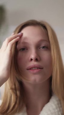 Vertical video. Clean face model. Morning beauty. Facial care. Confident satisfied girl with radiant skin touching healthy shiny hair on light background.