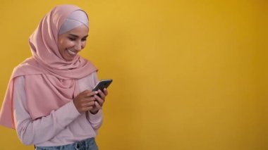 Gadget kullanıcısı. İnternette sohbet ediyoruz. İnternet iletişimi. Turuncu fotokopi arkaplanda izole edilmiş telefondaki tesettürlü mesajlı neşeli kadın..