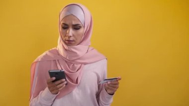 Ödeme hatası. Finansal sorun. İşlem başarısız oldu. Sarı boş arkaplanda izole edilmiş telefon kartı kullanan kafası karışmış tesettürlü kadın..