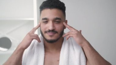 Yaşlanma karşıtı cilt bakımı. Yüz nemlendirici. Sabah bakımı. Kendine güveni tam bir adam banyonun iç tarafında gözlerinin altına yüz kremi sürüyor..