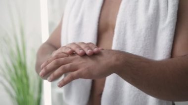 Hand moisturizing. Dry skin treatment. Dermatology care. Unrecognizable shirtless man applying lotion from tube on light defocused background.
