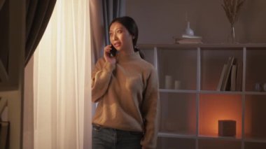 Telefon konuşması. Mobil iletişim. 5G ağ bağlantısı. Rahat, neşeli kadın modern ev içi oturma odasında keyifli sohbetler ediyor..