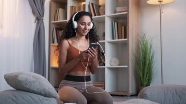 Phone playlist. Gadget entertainment. Music app. Cheerful dancing woman in headset listening song on smartphone on living room floor at home.