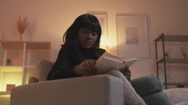 Kitap sever. Ev tatili. Edebiyat hobisi. Rahat, düşünceli, zeki bir kadın modern Hygge oturma odasındaki rahat koltukta ilginç bir roman okuyor..