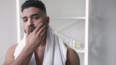 Sakal bakımı. Yüz bakımı. Hijyen rutini. Tatmin olmuş, yakışıklı, üstsüz bir adam banyoda duştan sonra sakallara dokunmaktan zevk alıyor..