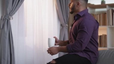 Sabah ilham geldi. Yeni bir gün. Ev tatili. Rahat, düşünceli adam sıcak çay içmekten zevk alıyor. Açık ev iç mekanına pencereden bakıyor..