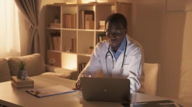 Doktor hatta. Teletıp görüntülü arama. Dijital klinik. Neşeli erkek hekim, modern iş yerinde dizüstü bilgisayar kullanarak hastaya danışmanlık yapıyor..