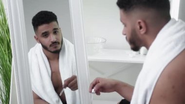 Sakal bakımı. Yüz bakımı. Sabah rutini. Kendinden emin, üstsüz bir adam aynanın yansıması olarak kirli sakallarından yağ sürüyor..