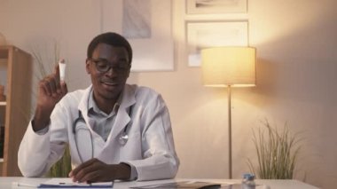 Doktor görüntülü arama. Tele sağlık danışmanlığı. Çevrimiçi tıbbi servis. Kendine güvenen erkek dermatolog modern iç mekanda krem tavsiye ediyor..