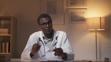 Doctor video chat. Telehealth consulting. Internet appointment. Confident male physician prescribing pills blister working late at modern home interior.