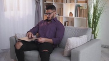 Mesafe öğrenme. Online eğitim. Uzaktan çalışma. Modern oturma odasındaki koltukta oturup dizüstü bilgisayar kullanan kendine güvenen zeki bir adam..