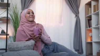 Kahve rahatlatıcı. Keyfin yerinde. İyi günler. Neşeli, keyifli, tesettürlü bir kadın evdeki sıcak oturma odasında bir fincan sıcak çay içiyor..