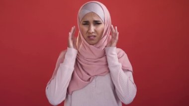 Migraine pain. Headache suffering. Health problem. Unhealthy sad woman in hijab massaging temples in ache tension isolated on red background.