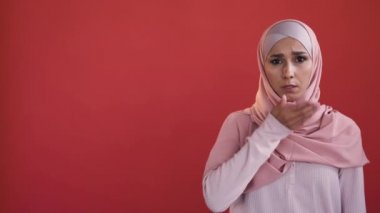Voice freedom. Cant speak. Female rights. Stressed scared speechless woman in hijab covering mouth with hand isolated on red copy space background.