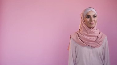 Smiling muslim woman. Islamic fashion. Veiled clothing. Happy attractive female model in elegant hijab outfit isolated on pastel pink copy space background.