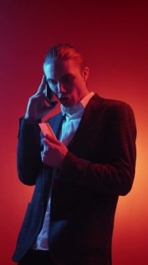 Vertical video. Bank conflict. Money scam. Financial fraud. Neon light frustrated annoyed angry business mad man with credit card yelling on phone isolated on red background.