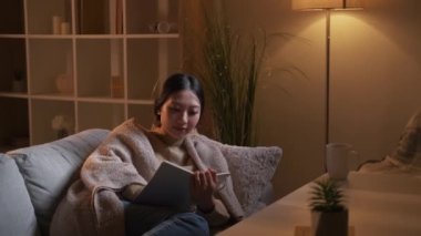 Sketching hobby. Creative home leisure. Weekend inspiration. Relaxed girl enjoying drawing in notebook on cozy couch in evening hygge living room interior.