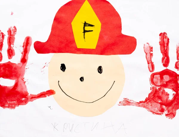 Kids art. Happy fireman. Creative improvisation. Artistic work of smiling face collage in professional firefighter cap and hand palms print red color.