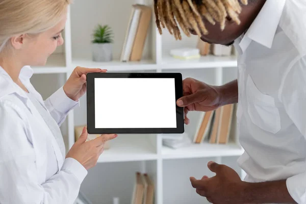 Virtual presentation. Office couple. Digital mockup. Unrecognizable smiling black man and woman holding tablet computer with blank screen in light room interior.