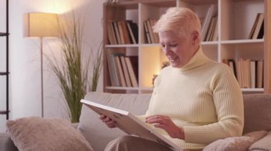 Happy memories. Family nostalgia. Senior widow. Dreamy sentimental mature woman holding frame talking to husband photo on couch at home living room.
