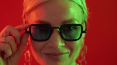 Playful woman. Flirty emotion. Neon light people. Closeup portrait of charming middle age female in stylish sunglasses winking eye in vibrant red glow.