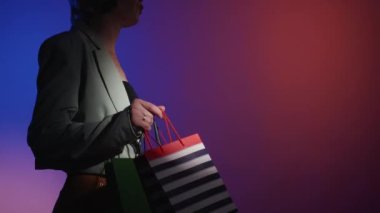Black Friday. Super sale. Shopping advertising. Unrecognizable fashionable woman customer with many shopper bags in multicolor neon light copy space.