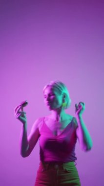 Dessert joy. Food pleasure. Joyful retirement. Funny happy senior woman eating delicious donut pastry dancing in bright neon light copy space vertical.